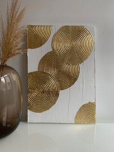 a white and gold art piece next to a vase with dried grass in front of it