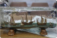 a glass bottle filled with miniature ships on top of a wooden table next to other items