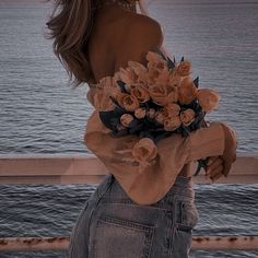 a woman is standing by the water with her back to the camera and holding a bouquet of flowers