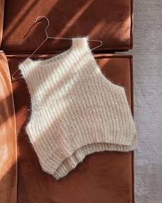 a sweater hanging on a clothes hanger next to a brown leather couch and chair