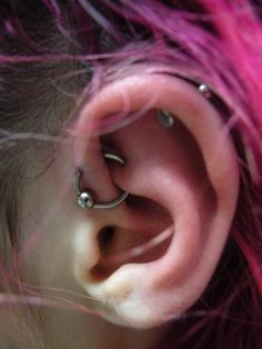 a person with pink hair has piercings on their ears and behind them is an ear ring