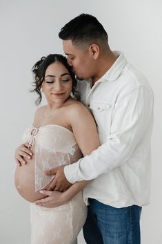 a pregnant couple cuddles and kisses while posing for their newborn photo session in the studio