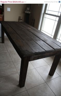 a wooden table sitting on top of a white tile floor next to a large window