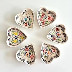 six heart shaped dishes are arranged in a circle on a white surface, each with different designs