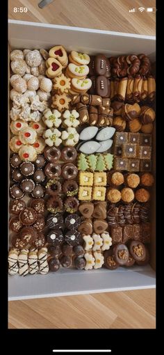 a box filled with lots of different types of donuts on top of a wooden floor