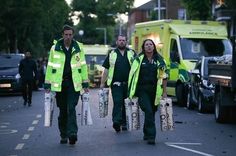 three emergency personnel walking down the street with their bags in hand and an ambulance behind them