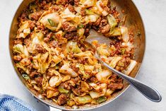 a skillet filled with cabbage and meat on top of a white counter next to a blue towel