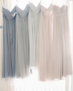 four different colored dresses hanging in front of a window