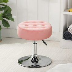 a pink stool sitting on top of a white floor next to a potted plant