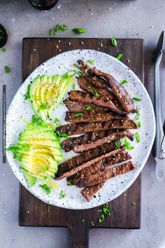 steak and avocado on a white plate with utensils next to it