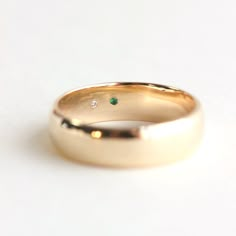 a gold wedding band with two diamonds on the top and one green stone in the middle