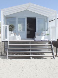 there is a small house on the beach with chairs and a potted plant in it