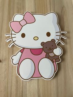 a hello kitty sticker with a teddy bear on it's chest, sitting on a wooden surface