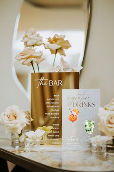 a table topped with flowers and cards next to a vase filled with white roses in front of a mirror