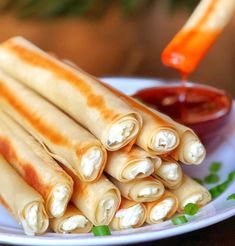 a plate with several spring rolls on it and dipping sauce in the bowl next to it