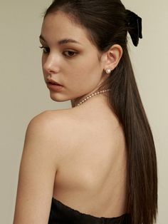 a woman wearing a black strapless dress with a bow in her hair, looking off to the side