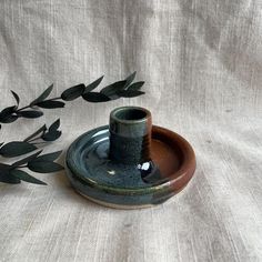 a green and brown vase sitting on top of a wooden tray next to a plant