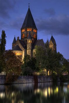 an old church lit up at night by the water with its reflection in the water