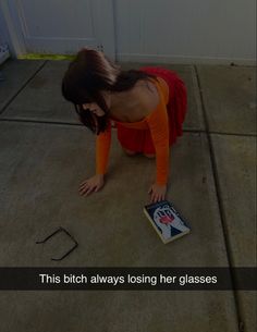 a woman in an orange shirt is looking at a book on the ground with her hands