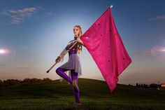 a woman holding a pink kite on top of a green grass covered field at sunset