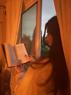 a woman reading a book while looking out the window