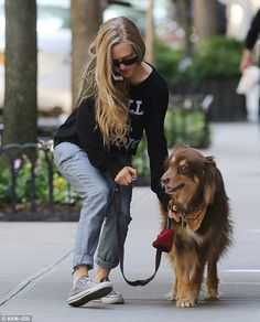 a woman is petting her dog on the leash while she walks down the street