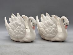 two white swans sitting next to each other on top of a gray surface with one swan facing the other way