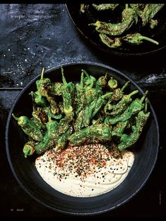 two black plates filled with green vegetables on top of a dark countertop next to a bowl of dip