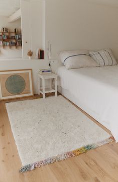 a bedroom with a white bed and rug on the floor next to bookshelves