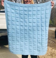 a woman holding up a blue blanket in front of her face while standing next to a white truck