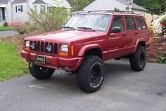 a red jeep parked in front of a house on a driveway next to some bushes