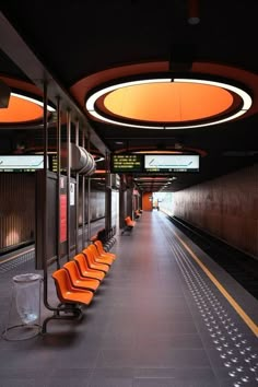 an empty train station with orange chairs and lights