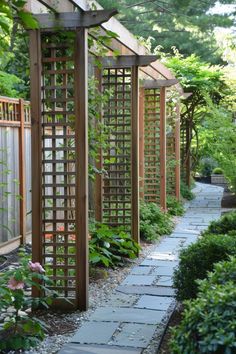 a stone path in the middle of a garden with wooden trelliss and plants