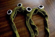 a crocheted frog hat with two eyes on it's head sitting on a wooden floor