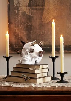 a skull sitting on top of some books with candles in front of it and a painting behind it