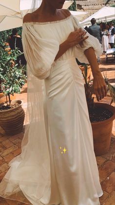 a woman in a white dress is standing under an umbrella with her hands on her hips