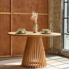 a wooden table with two cups and saucers on it in front of a window