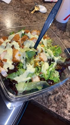 a salad in a plastic container on top of a counter with a blue handled utensil