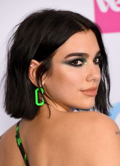 a woman with black hair and green eyeshadow wearing large earrings on her back