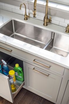 the kitchen sink is open and has cleaning products in it's cabinet drawer next to the faucet