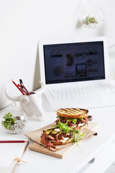 a sandwich sitting on top of a wooden cutting board next to a white laptop computer