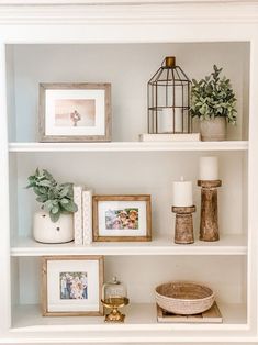 a shelf with pictures, candles and other items on it in a room that is white