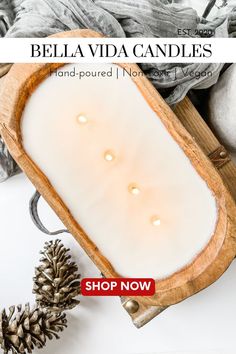 a wooden tray filled with white candles next to pine cones and other holiday decor items