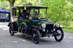 an old fashioned car driving down the road with trees in the backgrouund