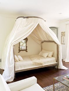 a white canopy bed sitting in the middle of a living room next to a couch