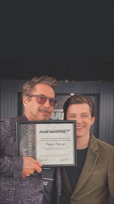 two men standing next to each other holding up an award plaque in front of them