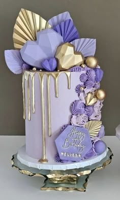 a purple and gold birthday cake with decorations on the top is sitting on a table