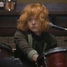 a woman with red hair is playing the drums