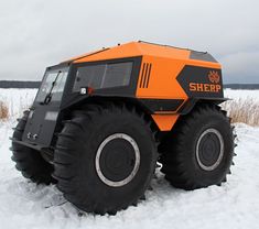 an orange and black truck is parked in the snow near some tall brown grass on a cloudy day