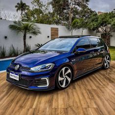 a blue volkswagen car parked in front of a house on a wooden floor next to a swimming pool